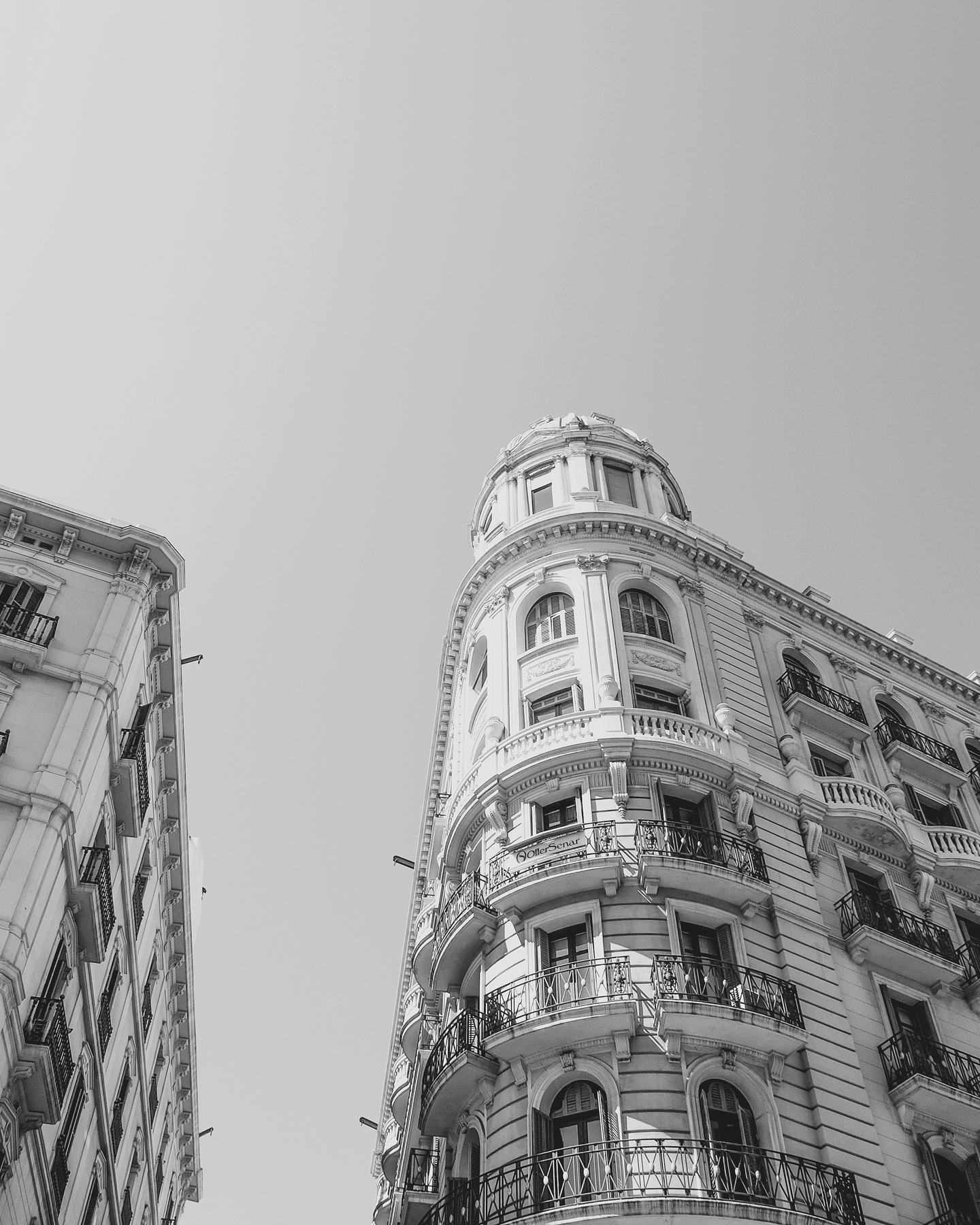 Two apartment buildings seen from the street, meeting an open sky